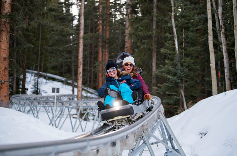 Two women riding down the Breathtaker Alpine Coaster in winter