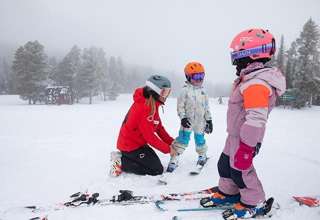 Ski school instructor helps child with ski clothes