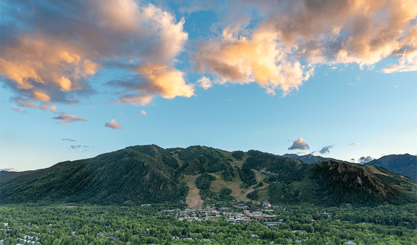 Long view of the town of Aspen in June, with the mountain in the background. It is very green and a nice sunset is in the background