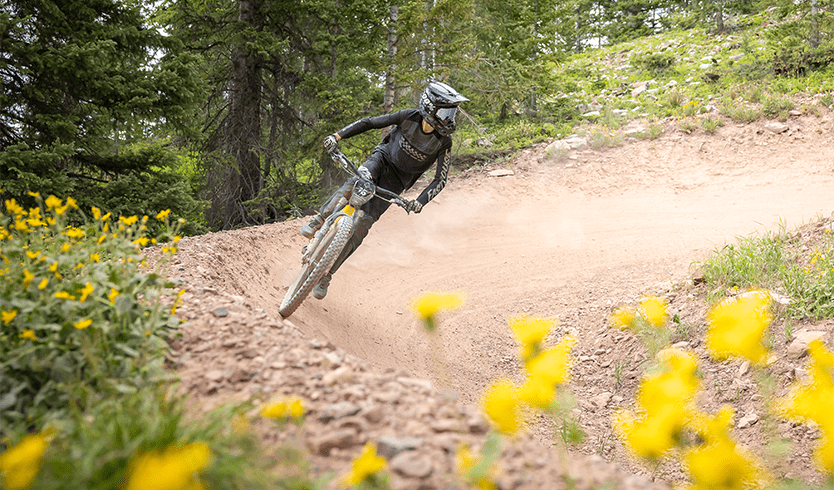 downhill biker takes a turn, with yellow flowers in foreground 