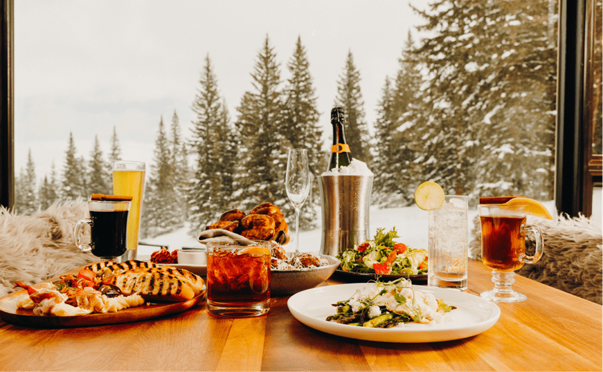 table spread at alpin room, warm drinks and dishes plated beautifully, falling snow through the window behind