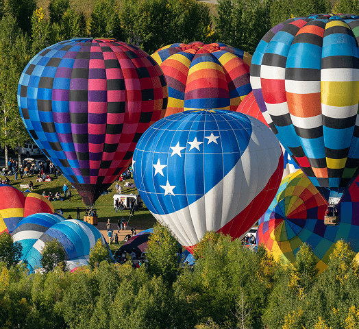 Hot air balloons rise above green and yellow trees  at snowmass balloon festival