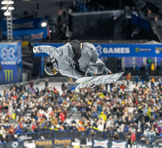 Snowboarder doing a tail grab on the halfpipe with the crowd watching in the background