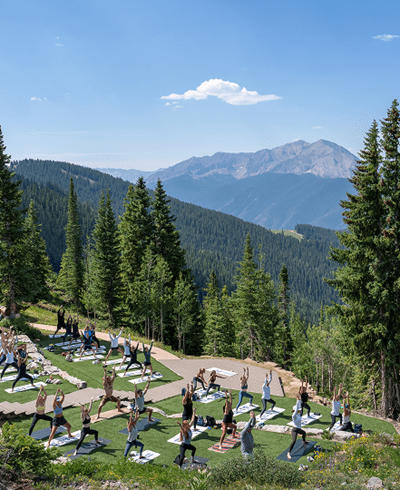 group of people do yoga atop aspen mountain in the summer, looking over the Aspen Valley