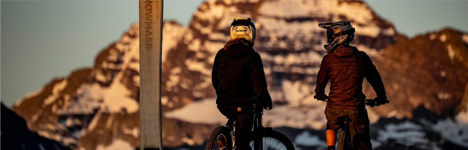 two people on mountain bikes look over the snowy peaks of snowmass