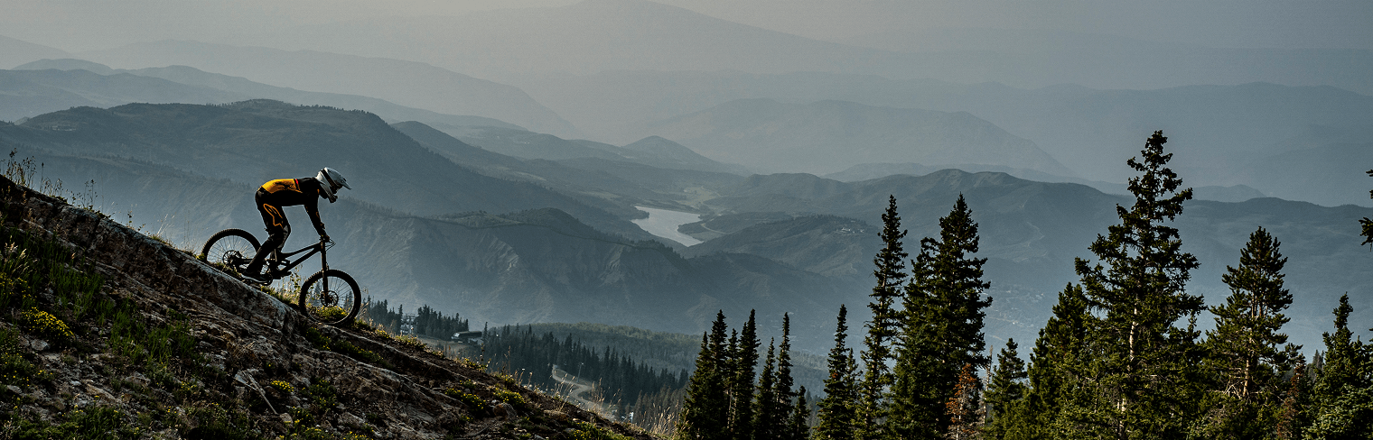 Biker going down trail with view of Aspen in backround