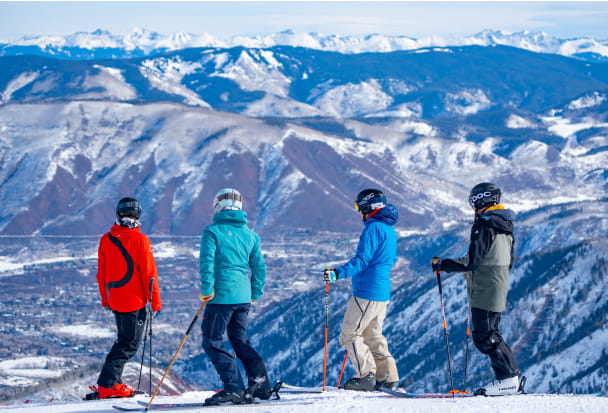 4 skiiers overlooking mountains on a ski slope 