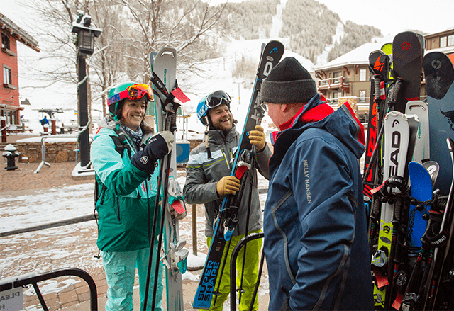 A group of skiers laughs together as they get ready to hit the slopes with all the proper gear