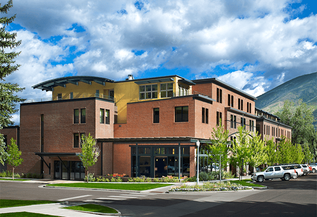 View of Limelight Aspen from the exterior, in the summer, mountains in background and summer flowers in foreground