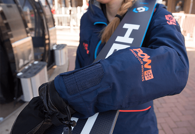 Woman loads Aspen Snowmass Gondola, focus on POW logo on her jacket arm