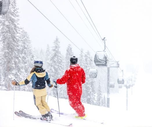 Two skiers standing under a gondola on a snowy day on a mountain