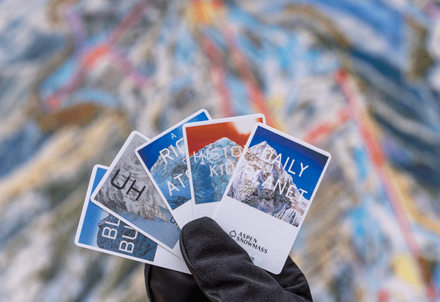 Person holds four lift tickets in front of aspen snowmass mountain map, displaying lift ticket art for 25-26 season