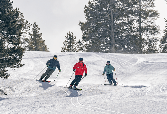 Two guests ski next to an Aspen Snowmass pro as they ski down a run at buttermilk