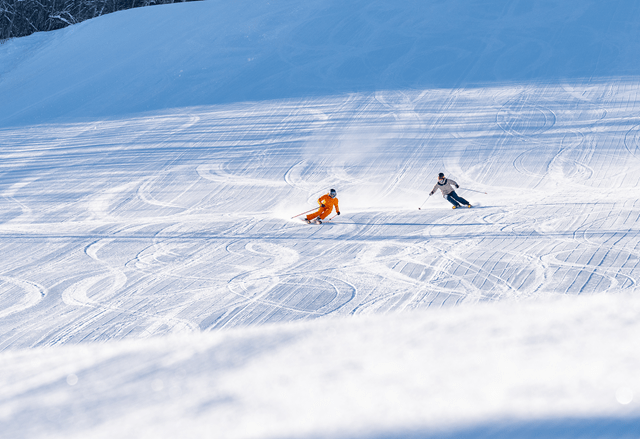 two skiers carve down an empty run during first tracks at snowmass