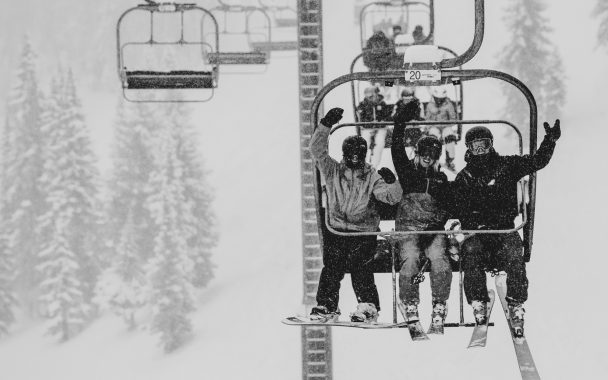 Black and white image of 3 skiers celebrating on a ski lift at aspen mountain