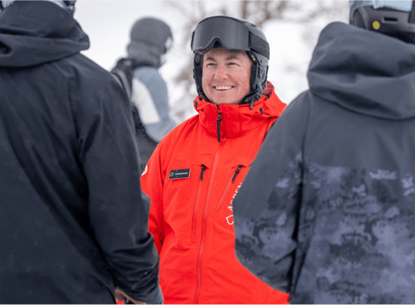 ski pro in his red ski jacket smiles at his two guests in black jackets