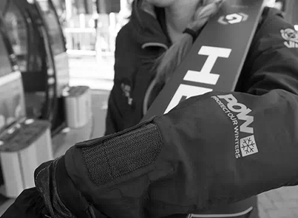black and white image of woman holding skis, POW logo on her jacket sleeve