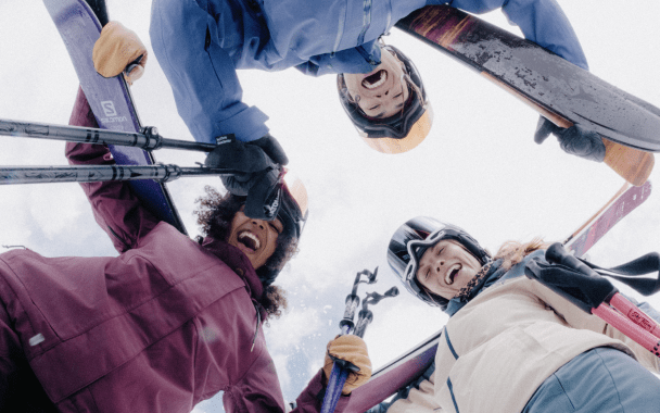 three woman look down at the camera from above in their ski gear on aspen mountain