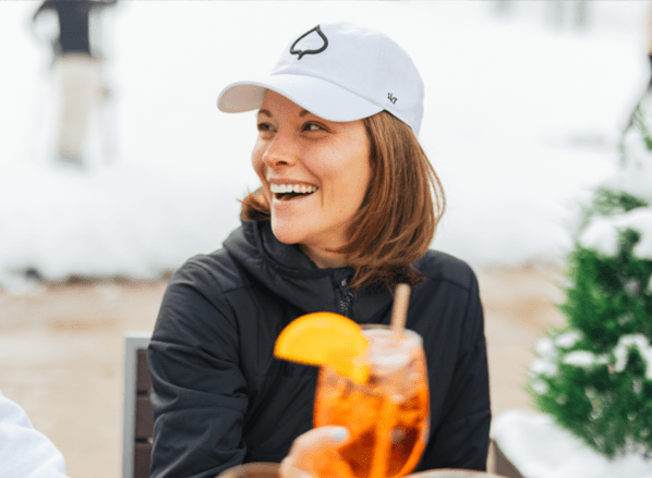 woman cheers her glass with aspen logo hat from aspen collection