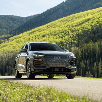 Black audi drives through green trees on dirt roads under blue summer skies in the Aspen Valley