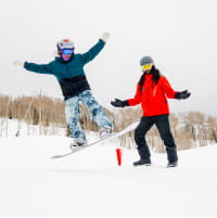 Young snowboarder jumping off a ramp with his ski pro watching