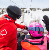 A child and ski pro sitting on a chairlift above a ski slope