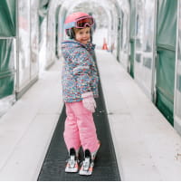 Girl in pink ski outfit on a conveyor belt with skis on