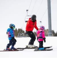 Two young kids enjoying a ski lesson witha  ski pro on a mountain