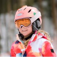 Close-up of a young girl's face in a ski outfit, goggles and pink helmet