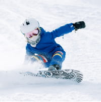 Child in blue ski suit snowboarding down a ski slope