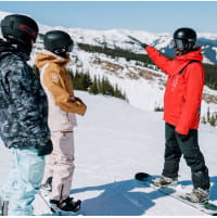 Two snowboarders watching a ski pro explain on a mountain