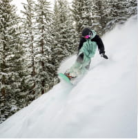 Snowboarder in black and green outfit carving on a steep slope
