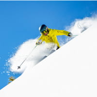 Skier in yellow outfit skiing through powder on a blue sky day