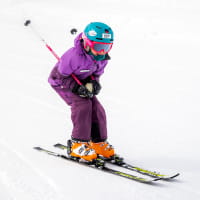 Child in purple ski outfit skiing down a slope