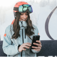 Woman in brightly colored ski gear in the Aspen Gondola looks at the Aspen Snowmass app on her phone