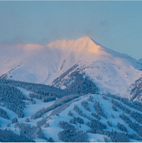 Aspen Snowmass from a distance, ski runs lined by snowy trees and tall peaks in the background