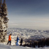Three people stand on the slopes of Aspen Snowmass looking out over the Roaring Fork Valley