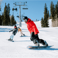 snowboarding pro leads two boarders down the mountain on a sunny day at snowmass