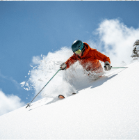 Skier pole plants in deep powder as it kicks up behind him, on a blue bird day