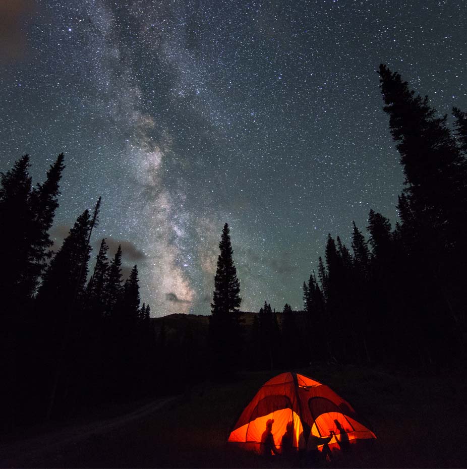 a tent lit up at night with trees and stars in the sky