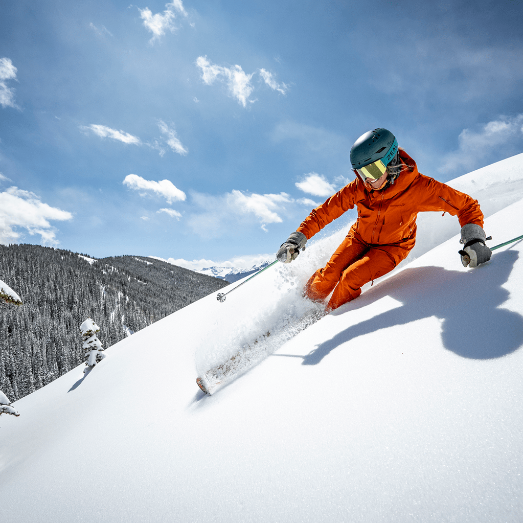 Woman in red ski suit carves down a fresh powder on a bluebird day