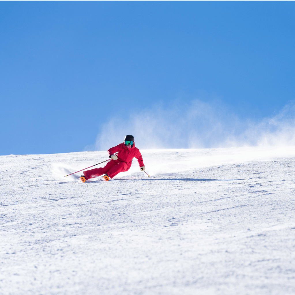 skier in all red ski suit carves deeply into a turn on an empty groomed run at aspen snowmass, blue skies above the white run
