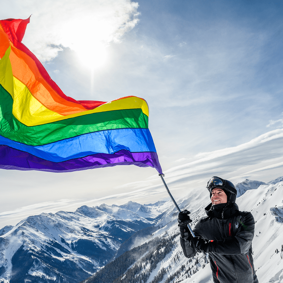 Single man holds a large LGBTQ+ above his head on the tip of the Highlands bowl