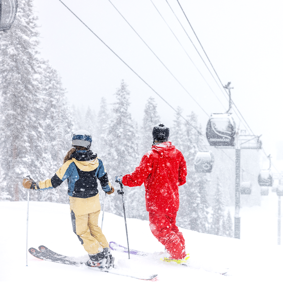two skiers stand under the gondola at Snowmass as snow falls on them on a winter day