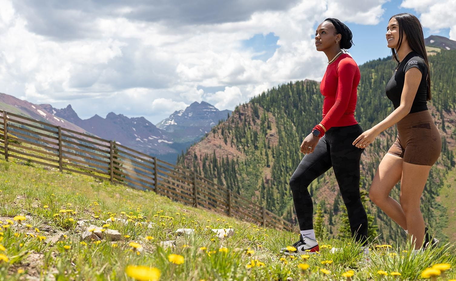 Two friends hike amidst the wildflowers atop Snowmass with views of Maroon Bells in the distance