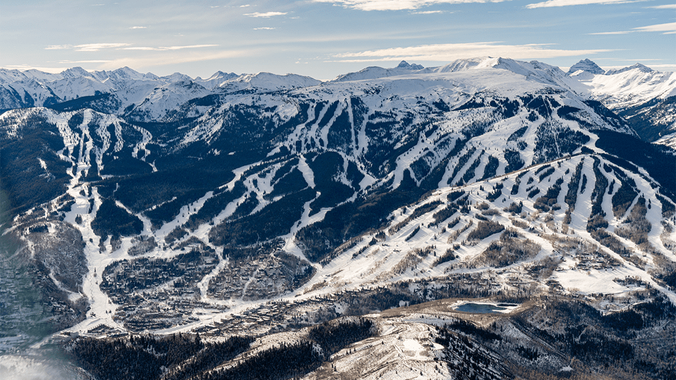 Aerial view of the four mountains at Aspen Snowmass, in the winter. White slopes and green pine trees on a blue bird day