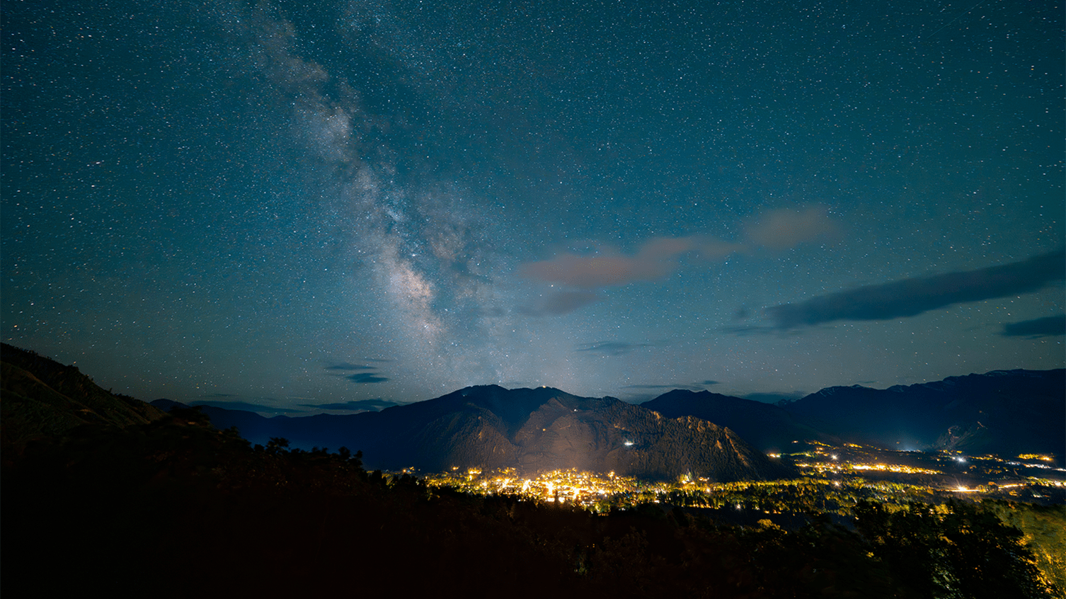 The town of Aspen in the summer, at night. The town is glowing and the milky way is glowing above