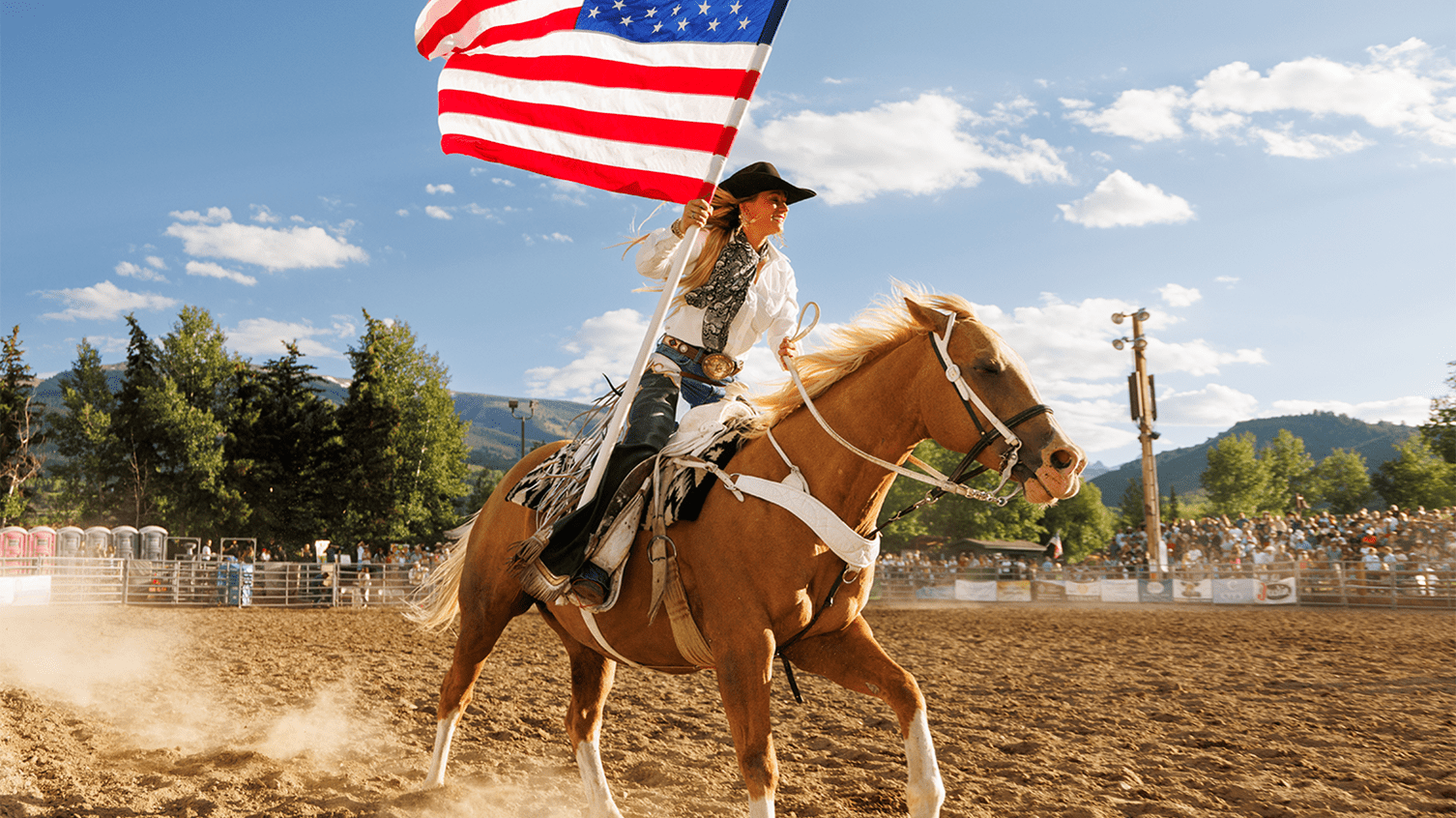 Rider circles arena on tan horse, waving American flag