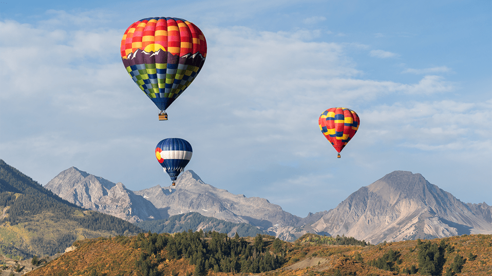 Three hot air balloons rise over Snowmass, in the fall, as Daly Peak rises majestically in the background
