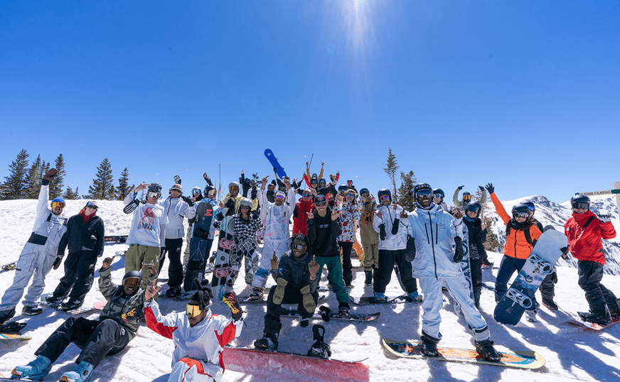 Crowd of people smile for the camera on a bluebird day, on the snowy slopes of Snowmass ski resort, for burton's culture shifters event, brining diversity onto the ski hill